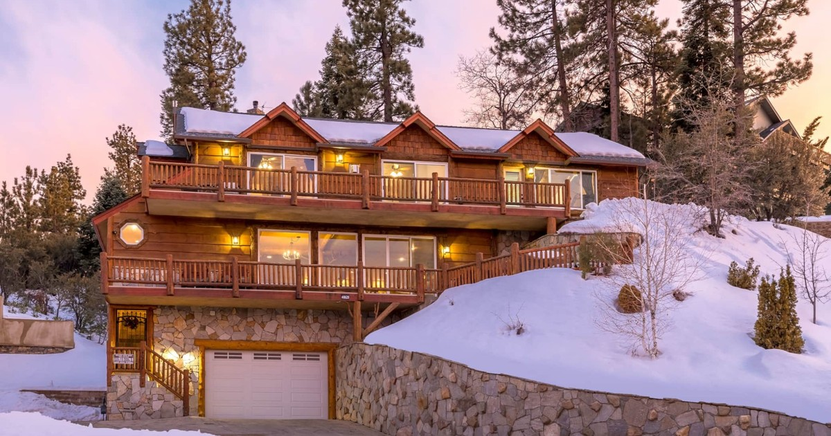 Snow-covered mountain home in Big Bear Lake, California with elevated wood decks and pine trees